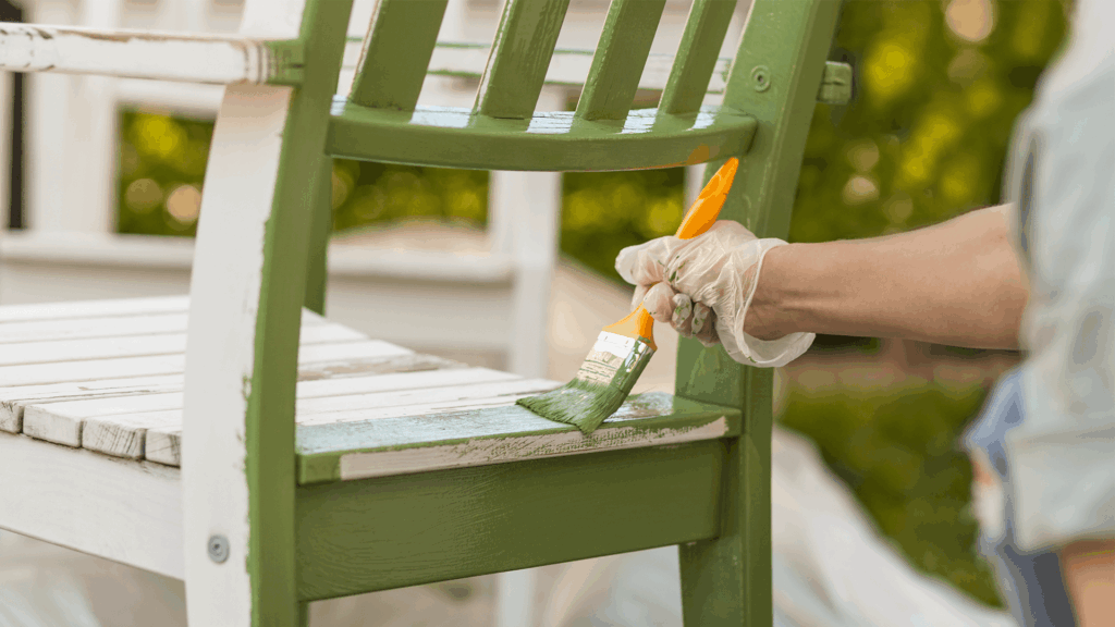 person painting a wooden chair green with a paintbrush