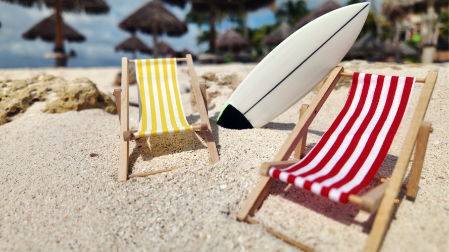 Two striped sling chairs sitting in the sand with a surf board