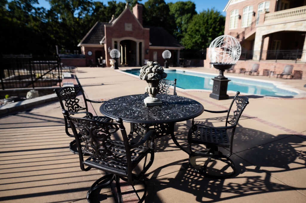 Cast aluminum outdoor dining set with detailed scrollwork restored in a satin black finish on a luxury poolside patio.